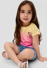 Korte mouwen gradient t-shirt in geel naar roze met een ananasafbeelding. Gecombineerd met denim shorts en lichte sandalen. Haar is lang en bruin.