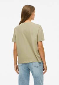 Olijfgroen t-shirt met korte mouwen, een relaxte pasvorm, ronde halslijn en zachte textuur; gecombineerd met lichtblauwe jeans.