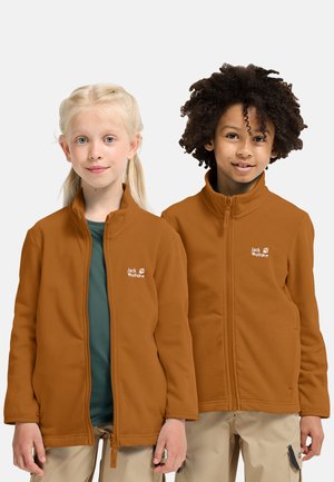 Deux enfants portant des vestes en polaire marron Jack Wolfskin et des pantalons beige, debout côte à côte sur un fond uni.