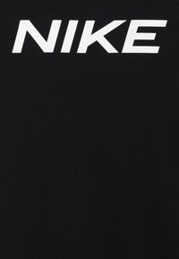 Tejido negro que presenta un gran logo blanco de "NIKE" en la parte frontal. El material parece suave con un acabado mate.