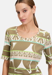 Short-sleeve top featuring a brown, ribbed texture with geometric patterns in cream, green, and blue stripes. Scoop neckline and fitted design.