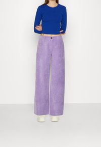 Tajt blå kortärmad topp i kombination med högmidjade, vida lavendelfärgade kordbyxor som har knäppning och strukturerad textil.