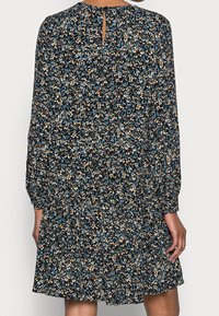 Robe noire à manches longues, motif floral en bleu, blanc et orange. Présente une taille froncée et un détail en trou de serrure au dos.