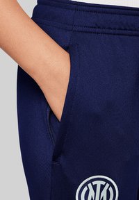 Navyblauwe joggingbroek met een gladde textuur, voorzien van een zijzak en een cirkelvormig logo in wit en navy op de dij.
