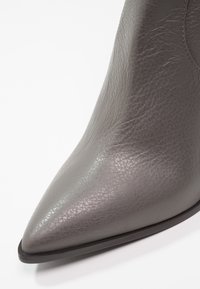 Bottine en cuir gris avec un bout pointu, texture lisse et silhouette effilée. Brillance subtile et détail de couture le long du bord.