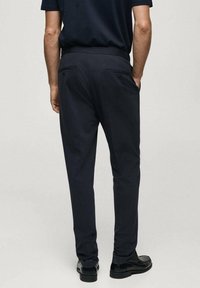 Pantaloni scuri navy su misura con una texture liscia, vestibilità slim e due tasche posteriori, abbinati a scarpe nere.