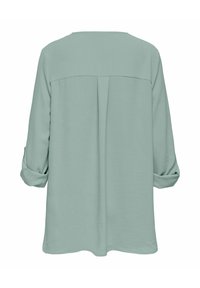 Blouse vert clair à manches longues avec poignets retroussés et pli central au dos, vue de dos sur fond blanc.