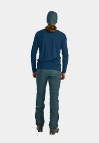 Blue long-sleeve shirt, green pants with side zippers, and black boots. The design is functional for outdoor activity, featuring a smooth texture.