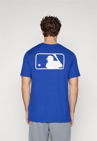 Királyk�ék pamut póló rövid ujjakkal, nagyméretű fehér baseball játékos sziluett grafikával a hátsó oldalon és kerek nyakkivágással.