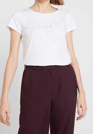 Witte T-shirt met korte mouwen en een lichtblauw rond logo in het midden met daarop de tekst "Roxy Authentic 1990", gecombineerd met donker bordeauxrode broeken.