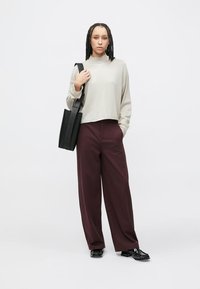 Jasnoszara, długorękawowa bluzka; luźne bordowe spodnie; czarna torba typu tote z paskiem; czarne buty z fakturowanym wzorem; neutralne tło.