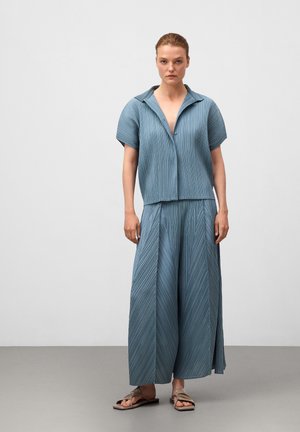Ensemble deux pièces plissé bleu clair composé d'un haut à col et manches courtes et d'une longue jupe fluide. Texture verticale notable et coupe décontractée.