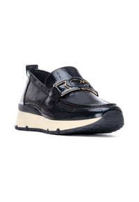 Zapatos de charol negros tipo slip-on con una textura brillante, que cuentan con un emblema dorado en la correa y una suela blanca contrastante con dibujo texturizado.