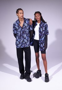 Camicie a maniche corte abbinate in nero con motivi astratti blu, abbinate a un top bianco e pantaloni corti neri, completate da sneakers nere.