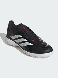 Μαύρο χαμηλό παπούτσι ποδοσφαίρου Adidas Predator με λευκές ρίγες, κόκκινες γραφικές λεπτομέρειες και λευκή σόλα σε ανοιχτό φόντο.