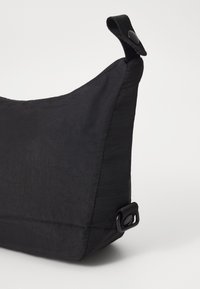 Čierna nylonová taška s textúrovaným povrchom, trojuholníkový tvar, horné uško a detail so zapínaním na cvok. Kompaktný a minimalistický dizajn.
