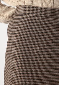Falda de tela de patrón espiga marrón con forma ajustada. La textura parece suave y tejida, presentando un sutil contraste de color entre negro y beige.