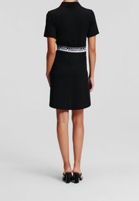 Svart kortärmad klänning med krage och ett märkesband av elastiskt material i midjan, med en rak skärning som slutar ovanför knäna.