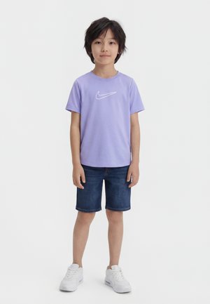 Dreng stående iført en lyse lilla Nike t-shirt, mørkeblå denimshorts og hvide sneakers mod en hvid baggrund.