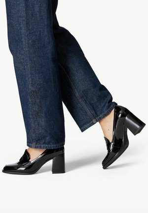Schwarze lacklederne Absatzloafer mit quadratischer Spitze und dekorativem Riemen, kombiniert mit dunkelblauen weitgeschnittenen Jeans.