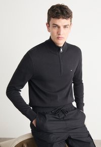 Svart zip-up genser med høy krage og ribbestrikkede mansjetter, kombinert med elastic waist cargo bukser i matchende svart farge.