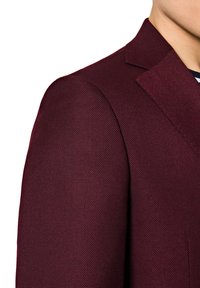 Burgundowy żakiet z teksturowanej tkaniny, z pojedynczym wycięciem klapy i miękkim krojem ramion. Skupienie uwagi na szwie ramion i detalu tkaniny.