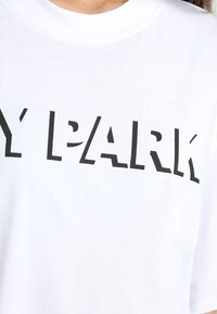 Camiseta de algodón blanca con letras negras en bloque que dicen "MI PARQUE" en el pecho, con cuello redondo y mangas cortas.