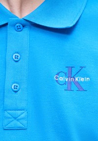 Φωτεινό μπλε πόλο πουκάμισο με τρία κουμπιά και κεντημένο λογότυπο Calvin Klein στο στήθος.