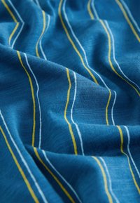 Tissu bleu avec tricot texturé et fines rayures verticales jaune et blanc, présenté avec des plis et des rides doux.