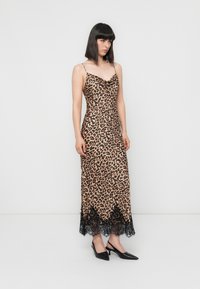 Vestido maxi com estampado de leopardo, decote drapeado, alças finas e barra de renda preta. Usado com sapatos de salto agudo pretos.