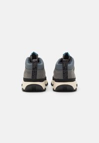 Zapatos de senderismo grises con acentos azules, material texturizado, un collar alto y una suela negra robusta que presenta un patrón de tracción distintivo.