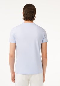 Camiseta de manga corta azul claro hecha de un tejido suave, con un corte ajustado y escote redondo, mostrada desde la parte de atrás.