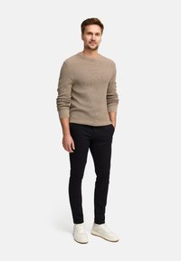 Beige gerippter Pullover, schwarze Slim-Fit-Hosen und weiße Sneakers. Der Pullover hat einen Rundhalsausschnitt und lange Ärmel mit aufgeschlagenen Bündchen.