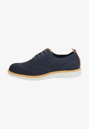 Scarpa in maglia blu navy con suola chiara, dettagli marroni, sei fori per i lacci e cuciture a contrasto. Design semplice, forma moderna.
