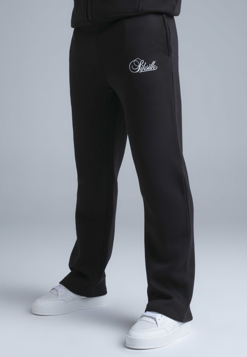 Pantalon de survêtement noir avec poches latérales, arborant un logo brodé blanc. Matière douce, coupe droite et taille côtelée.