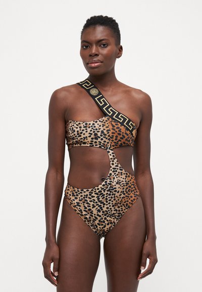 Maillot de bain une pièce à motif léopard, présentant un design découpé et une bretelle asymétrique avec un motif géométrique noir et or. Texture lisse et brillante.