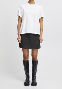 Vit bomull t-shirt med korta ärmar, i kombination med en mörkgrå minikjol och knähöga svarta läderstövlar med tjock sula.