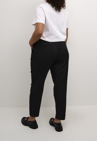 Pantalon noir fuselé avec une texture lisse, deux poches arrière et des détails sur les côtés. Assorti à un t-shirt blanc uni à col rond et des chaussures noires.