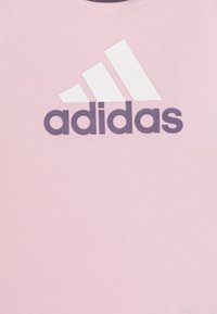 T-shirt di cotone rosa con logo Adidas bianco e grafica con tre strisce bianche sul petto. Collo rotondo, texture liscia.
