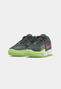 Grijze sportschoenen met een mesh bovenwerk, levendige groene accenten, een rode Nike-logo, een getextureerde buitenzool en een gevoerde kraag voor ondersteuning.