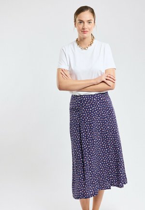 Jupe navy avec un imprimé floral rouge et blanc, dotée d'une coupe évasée et d'un tissu léger, associée à un haut blanc à manches courtes.