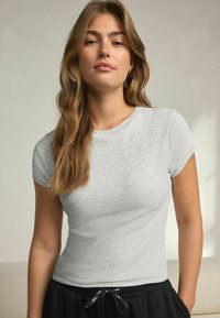 Grå ribbad t-shirt med kort ärm och rund halslinning, bärs med svarta byxor som har dragsko i midjan. Enfärgad, slät textur.