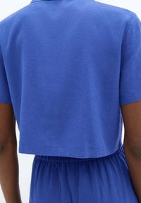 Persona che indossa un top blu corto a maniche corte e pantaloni abbinati blu con vita elastica, mostrata di spalle.