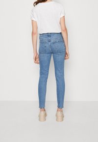 Vaqueros azul de talle alto hechos de denim, con un corte ajustado, bolsillos traseros y puños enrollados, combinados con zapatos de plataforma beige.
