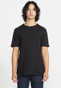 Sort kortærmet t-shirt med rund halsudskæring, har en lomme på venstre bryst og en diskret logo detalje på ærmet. Fremstillet af blødt stof.