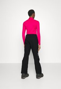 Fitted long-sleeve top in bright pink, paired with black pants featuring side zip pockets and white branding on the leg. Black footwear included.