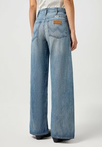 Breda jeans i ljusblå denim med hög midja, utsmyckade med en läderetikett på bakfickan, två bakfickor och diskreta sömnadsdetaljer.