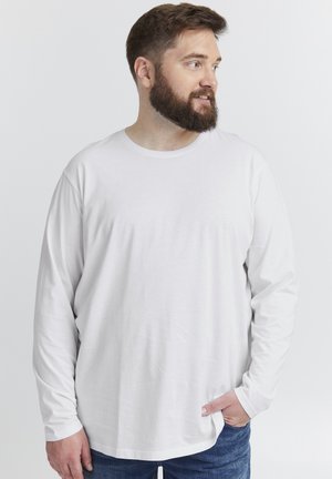 Langärmliges weißes Baumwoll-T-Shirt mit Rundhalsausschnitt, lockerer Passform und subtiler Textur, kombiniert mit dunkelblauen Jeans.