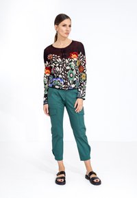 Pull en tricot avec un motif floral dans des couleurs vives sur un fond noir, associé à un pantalon cargo teal et des sandales noires.