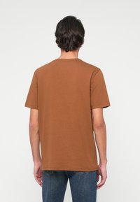 Rjava majica s kratkimi rokavi in okroglim izrezom, narejena iz mehkega bombaža, s preprosto teksturo in ravnim spodnjim robom.